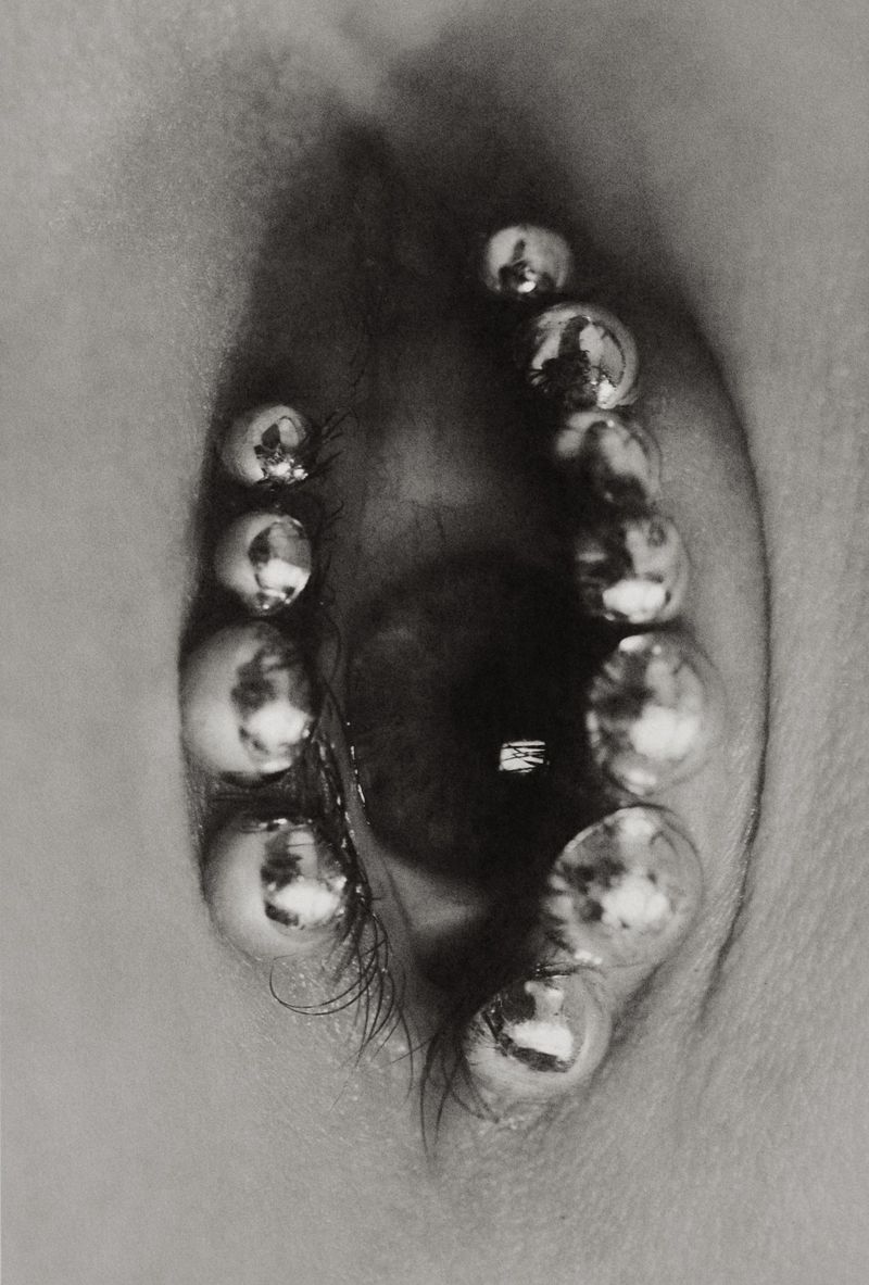 Close-up black and white photograph of an eye with numerous silver metal ball-shaped jewelry surrounding it.