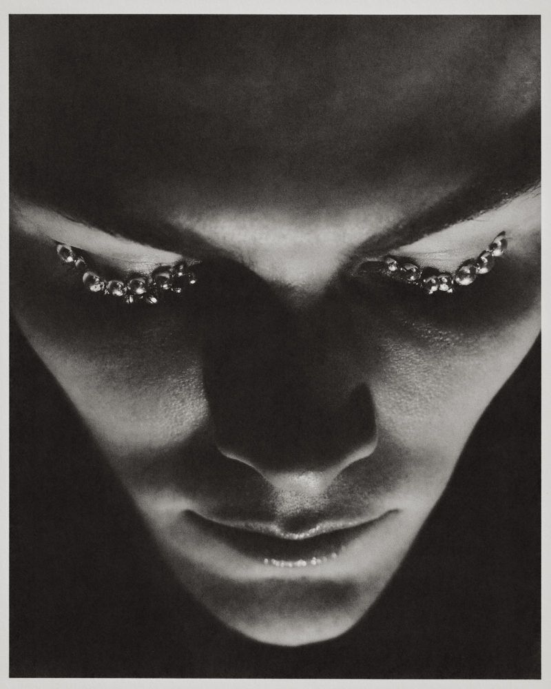 Monochrome close-up portrait of Trey Cunningham looking downward with reflective metallic bead embellishments under his eyes.