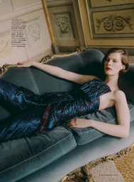 Model Hannah Weber reclines in a shimmering dark blue strapless bustier and matching trousers on a vintage velvet chaise lounge.