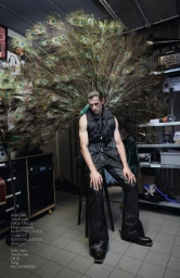 Model Kamil Skłodowski wearing a black puffer vest and wide-leg leather pants with a large peacock feather fan behind him.