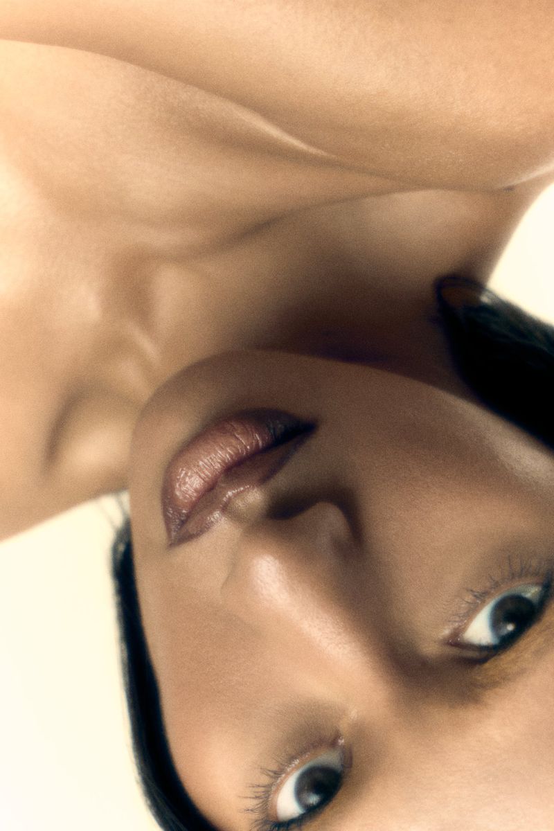 Close-up beauty portrait of a woman tilted upside down showcasing glossy lips and radiant skin against a pale background.