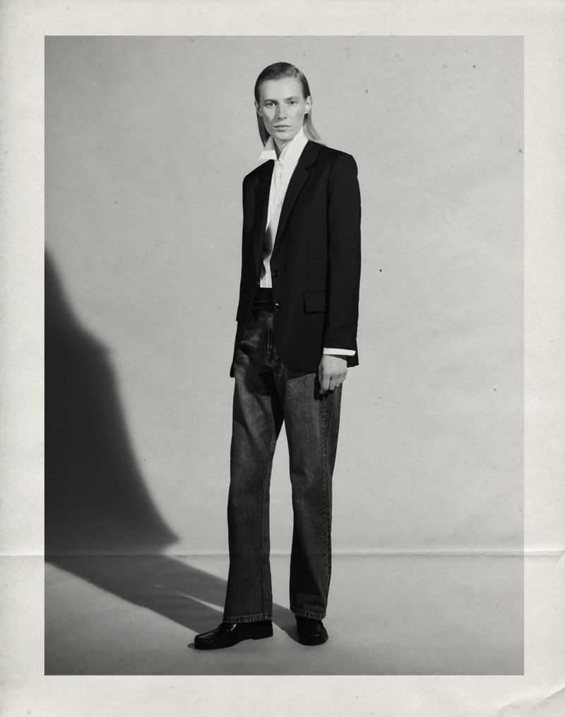 Julia Nobis wearing a black tailored blazer, white collared shirt, and dark straight-leg jeans in a studio portrait.
