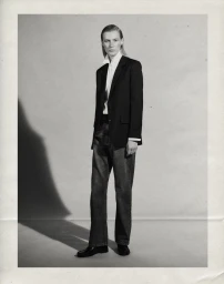 Model Julia Nobis standing in a tailored black blazer, white collared shirt, and denim jeans against a studio backdrop.