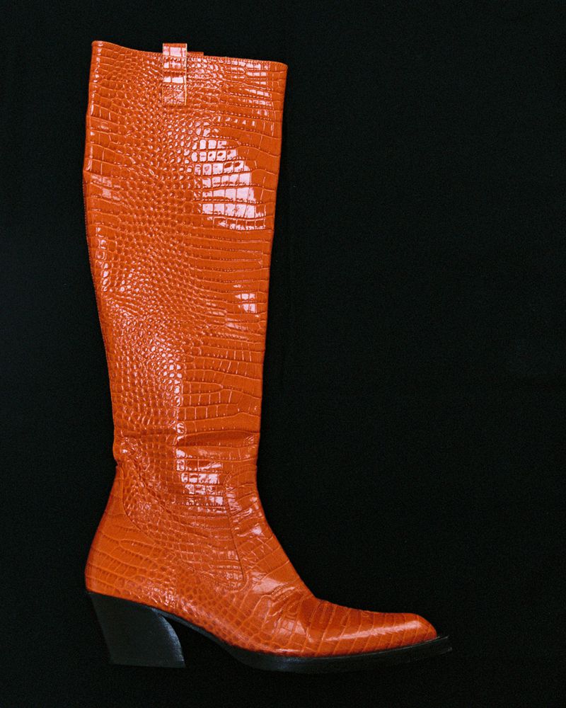 Orange crocodile-embossed knee-high leather boot with a Cuban heel displayed in profile against a solid black backdrop.