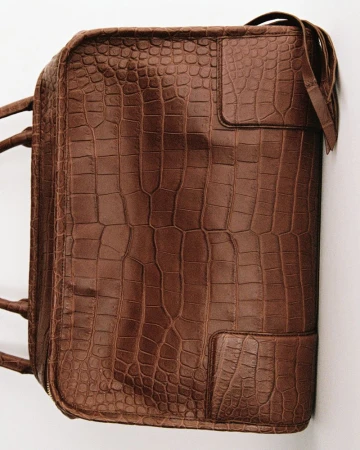 Brown crocodile-embossed leather travel bag with top handles and stitched leather details on a neutral studio background.