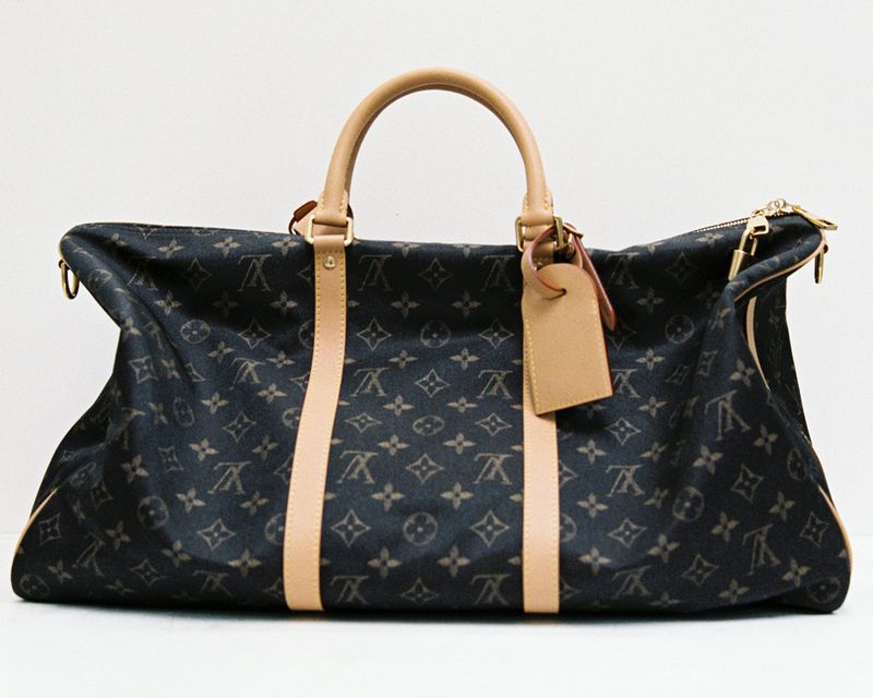 Monogram pattern duffle bag with beige leather trim and luggage tag on a white background.