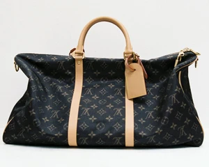 Monogram canvas travel duffle bag with light beige leather handles and luggage tag against a plain white background.