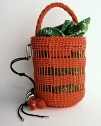 Orange woven bucket bag with a green patterned fabric pouch and decorative charm against a white background.