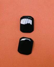 Pair of glossy black geometric earrings displayed vertically against a solid terracotta orange background.