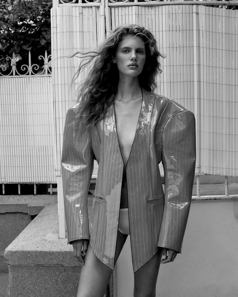 Model Rosalieke Fuchs wearing an exaggerated shoulder pinstripe vinyl blazer in front of a white slatted outdoor partition.