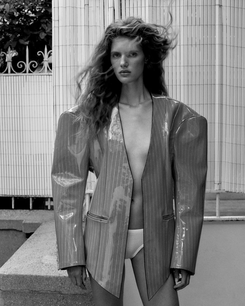 Model Rosalieke Fuchs wearing an oversized pinstripe vinyl blazer against an outdoor tiled wall.