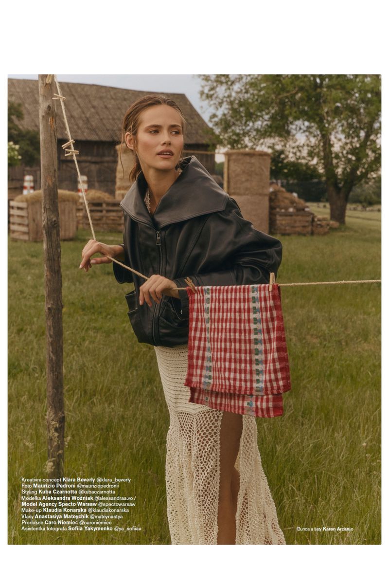 Model Alessandra Vo posing in a black leather jacket and cream crochet skirt behind a clothesline in a rural grassy field.