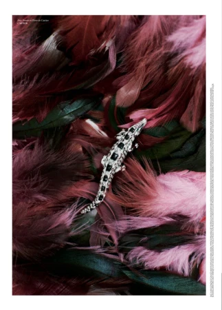 Diamond and black gemstone crocodile brooch resting on a bed of textured pink and burgundy feathers.
