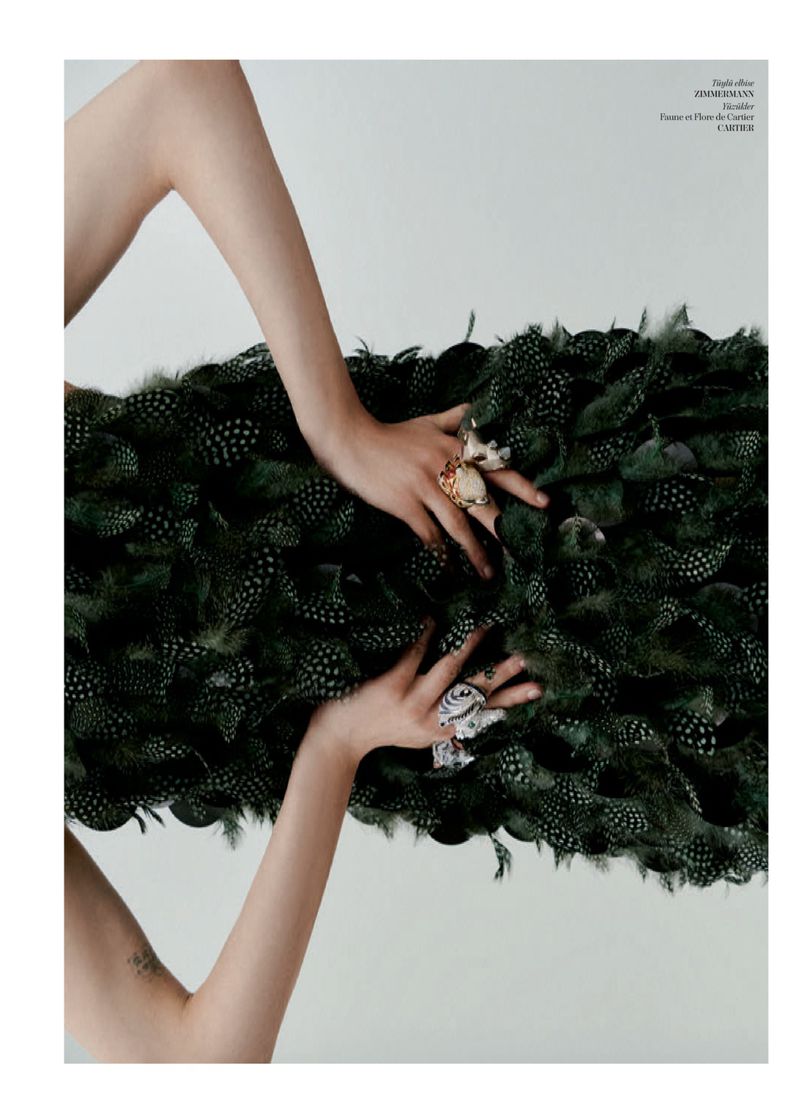 Model Patrycja Piekarska rests hands adorned with statement rings on a dark green feather garment against a white background.