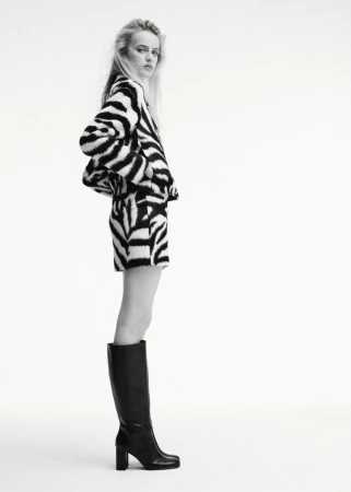 Model wearing a black and white zebra-print jacket and matching skirt paired with black knee-high boots against a white seamless backdrop.