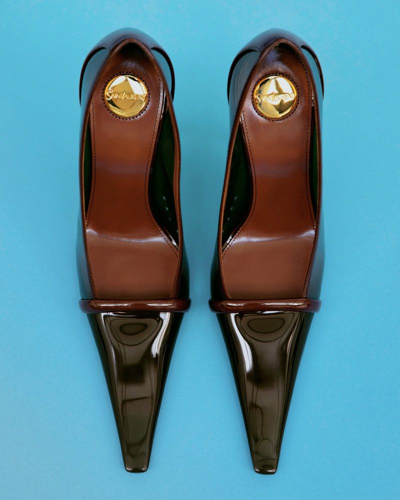 Top-down view of a pair of brown patent pointed-toe high heels placed symmetrically on a solid blue surface.