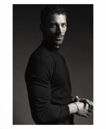 Monochrome studio portrait of model Simone Susinna wearing a black mock neck top with clasped hands against a dark background.