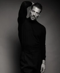 Monochrome portrait of model Simone Susinna wearing a black turtleneck and black trousers against a neutral studio backdrop.