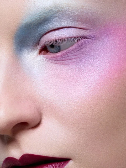 Close-up portrait of a woman's face with dramatic, colorful makeup in shades of blue, purple, pink, and red on her eyes and lips.