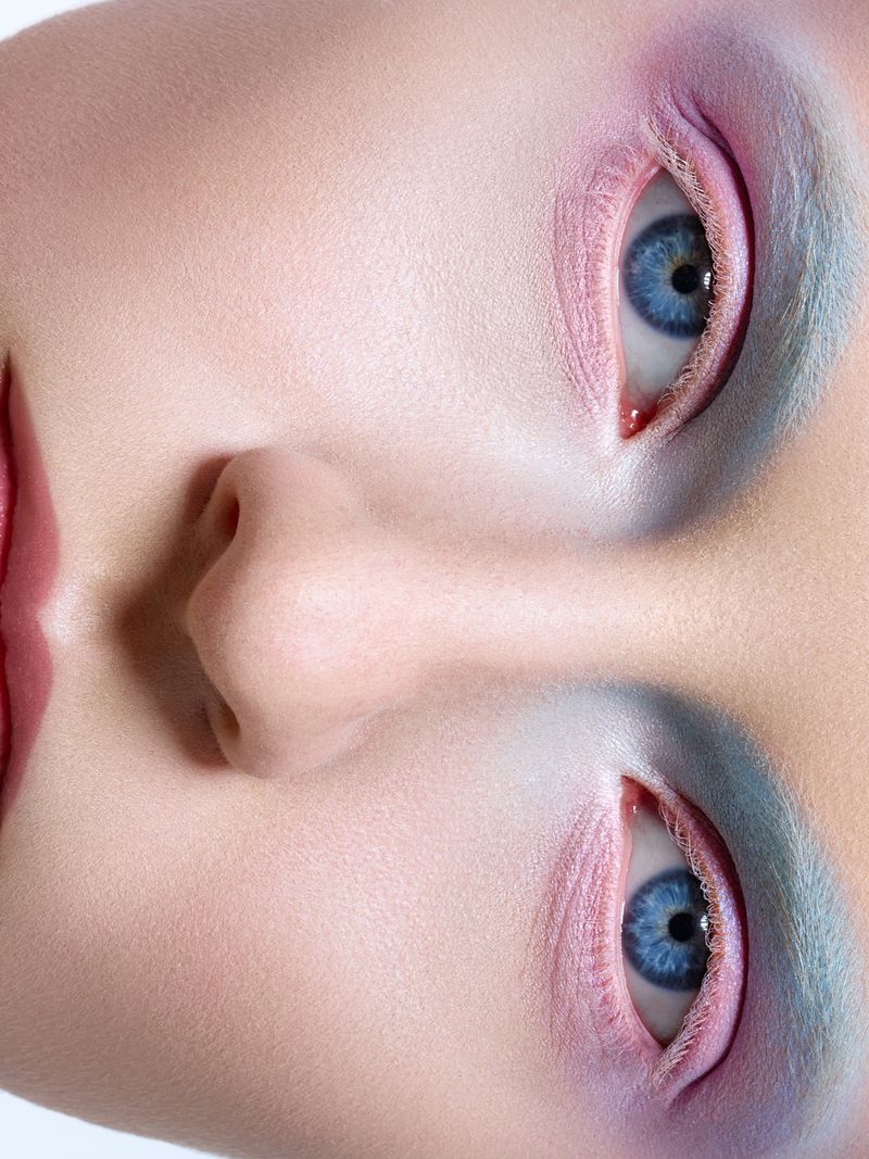 Macro beauty shot of a woman's face showcasing dramatic eye makeup and glossy lips in pastel shades, high-key lighting and smooth skin texture.