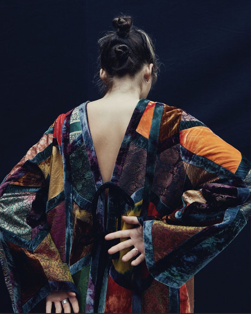 Back view of a woman with hair in a bun, wearing a multicolored velvet patchwork dress, showing the dress's design and texture.