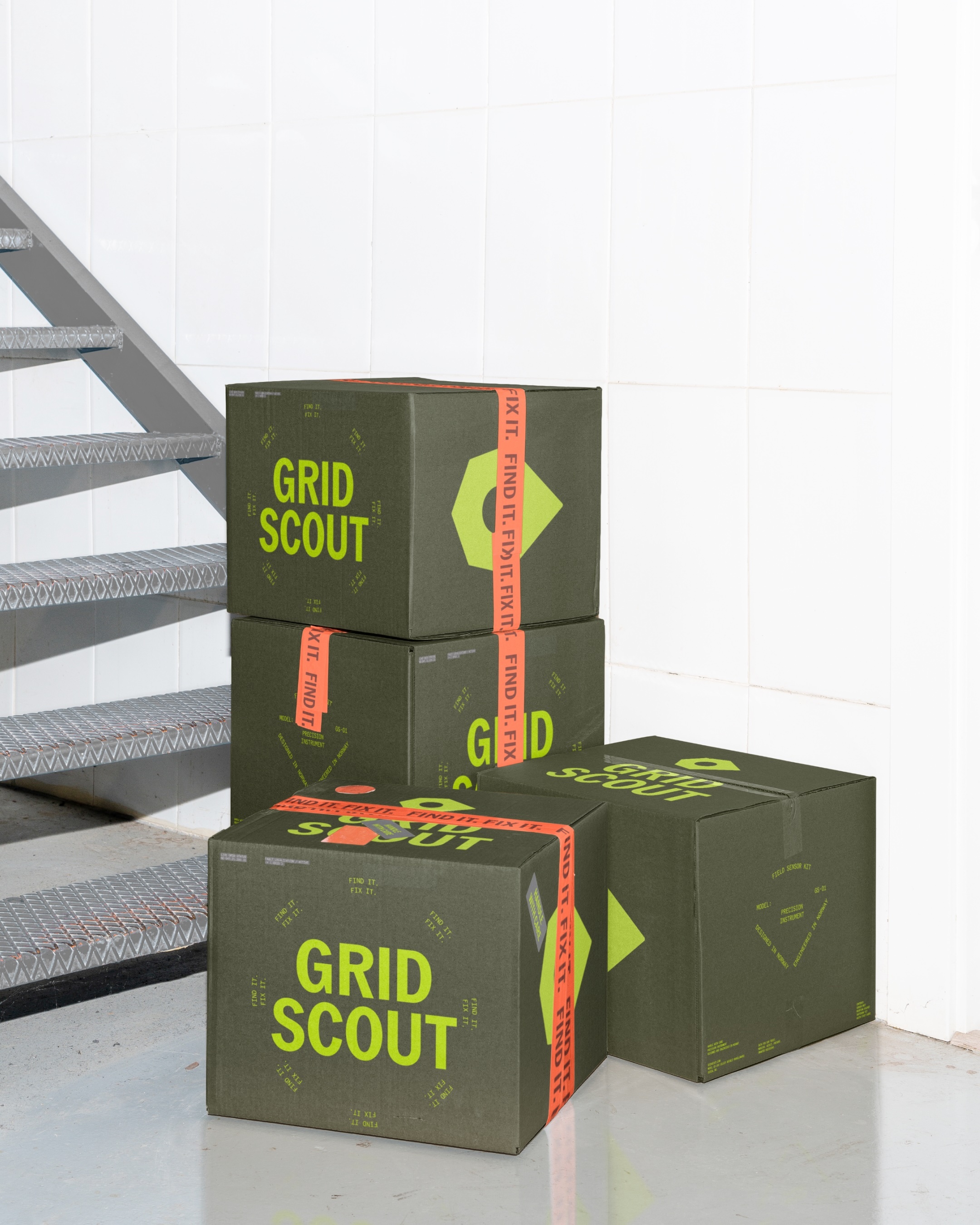 Branded olive green GridScout cardboard boxes stacked next to industrial metal stairs against a white tiled wall.