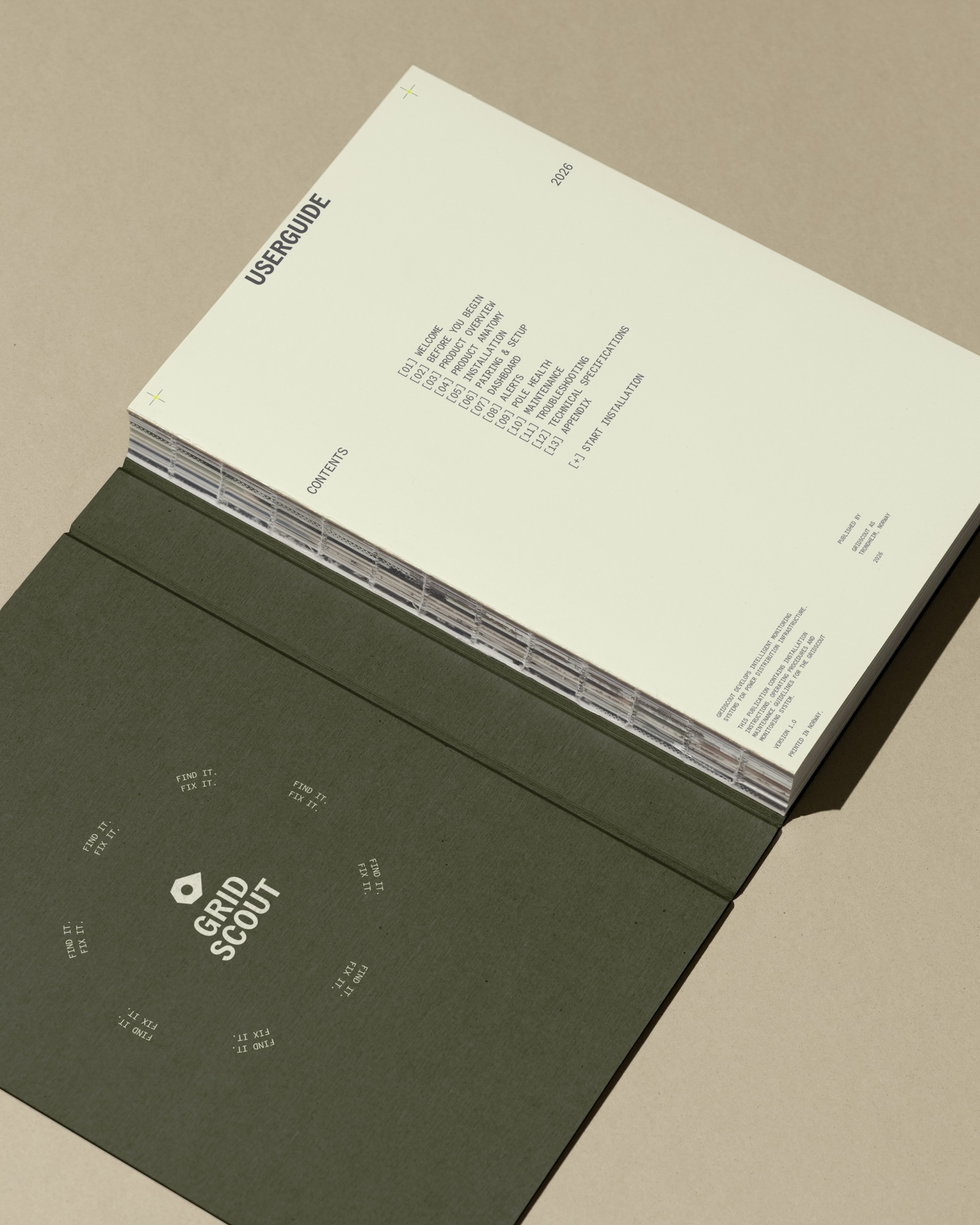Open GridScout user guide with an exposed thread-sewn spine, dark green cover, and cream contents page on a beige surface.