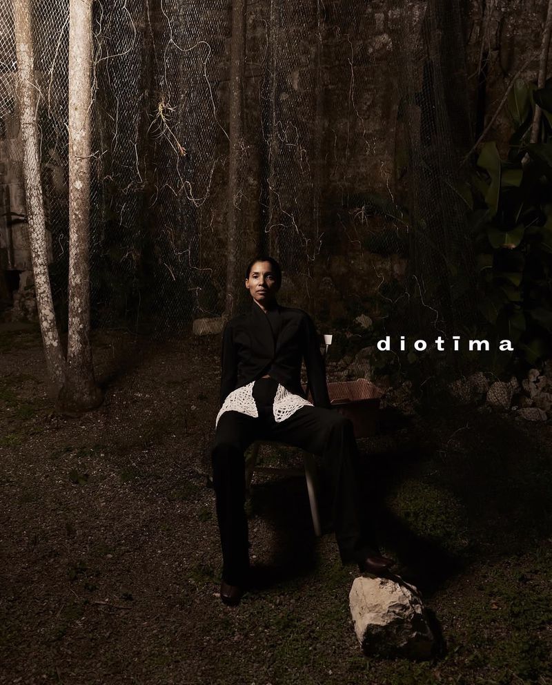 Model Romae Gordon seated outdoors at night wearing a black tailored suit with a white crochet waist detail for Diotima.
