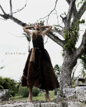 Model Romae Gordon in a textured brown midi dress posing with arms raised in front of an ancient tree outdoors.