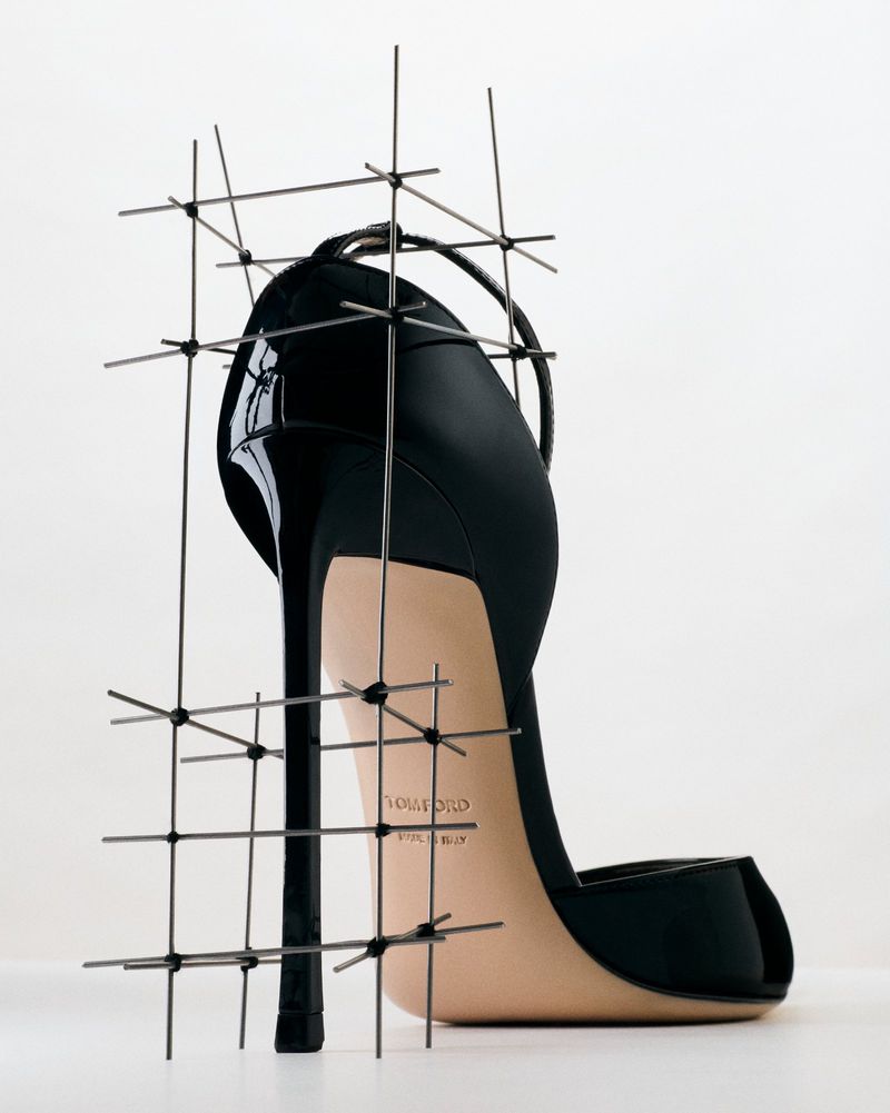 Black high-heeled stiletto pump enclosed in a delicate wire grid scaffold against a bright white background.