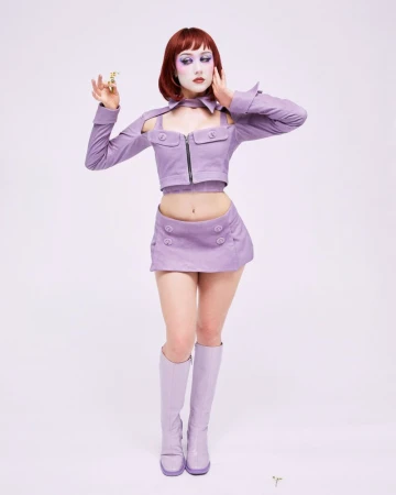 Chappell Roan posing in a lavender cropped top, mini skirt, and matching knee-high boots against a plain white studio backdrop.
