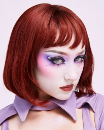 Chappell Roan with a red bob haircut and dramatic theatrical makeup wearing a lilac collared top against a pale backdrop.