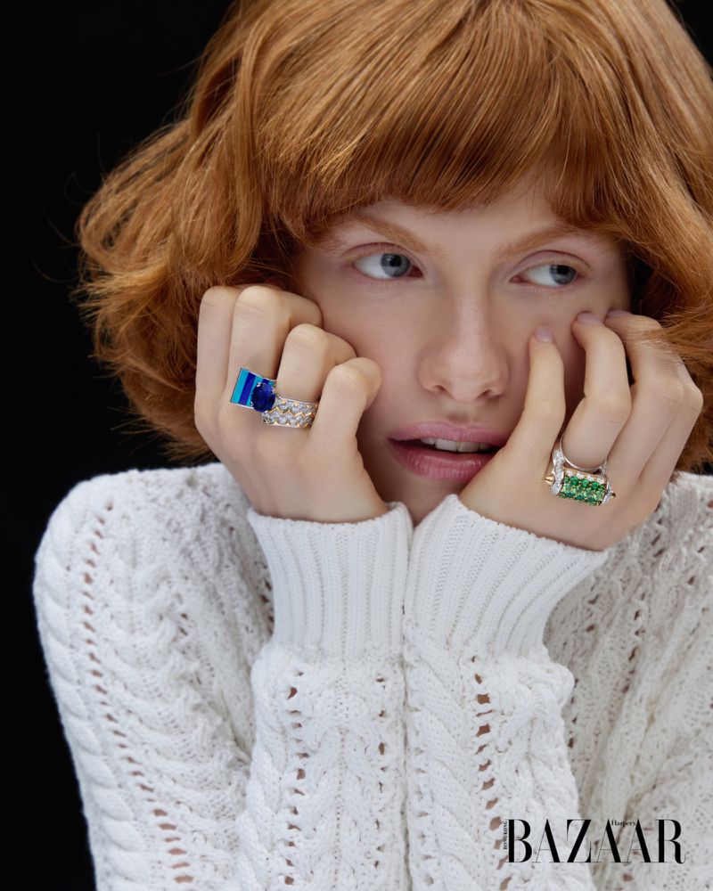 Model Edwina Preston wearing statement gemstone rings and a white cable-knit sweater against a black backdrop.