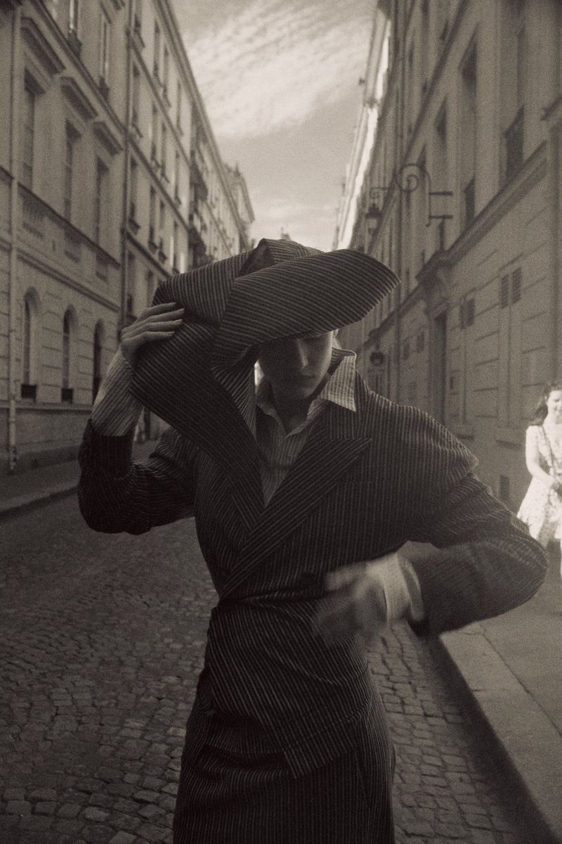 Model Mila Prvulovic poses in a pinstripe suit and sculptural hat on a cobblestone European street for Vogue Thailand.