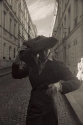 Model Mila Prvulovic poses in a pinstripe suit and sculptural hat on a cobblestone European street for Vogue Thailand.