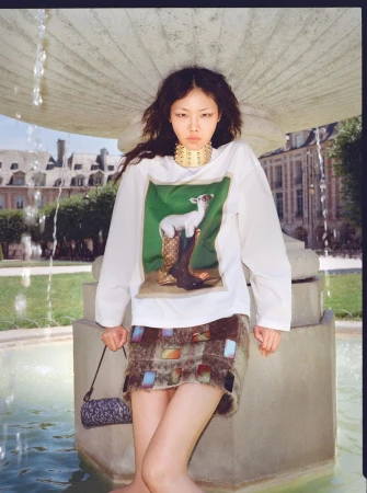 Model Sijia Kang posing in a white graphic long-sleeve top and patterned miniskirt in a stone fountain basin.