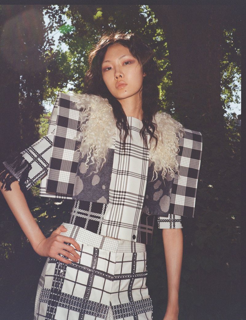 Model Sijia Kang posing outdoors in a black and white plaid jacket with exaggerated structured shoulders and cream shearling trim.