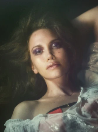 Close-up portrait of model Arina Maksimova with glossy purple eye makeup wearing a white ruffled off-the-shoulder top.