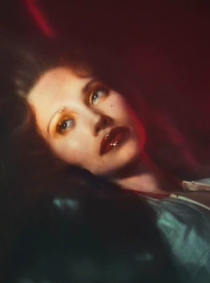 Close-up portrait of model Arina Maksimova featuring glossy dark red lips, yellow eyeshadow, and soft red-tinted ambient lighting.