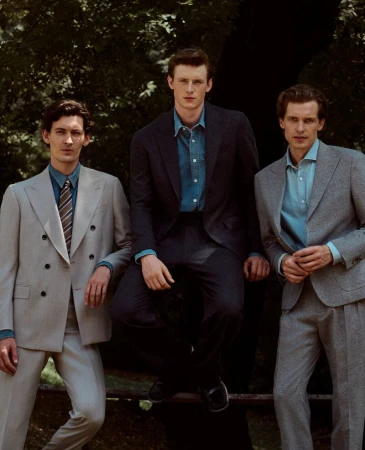 Three men in tailored suits and denim shirts posing outdoors against a leafy green background.