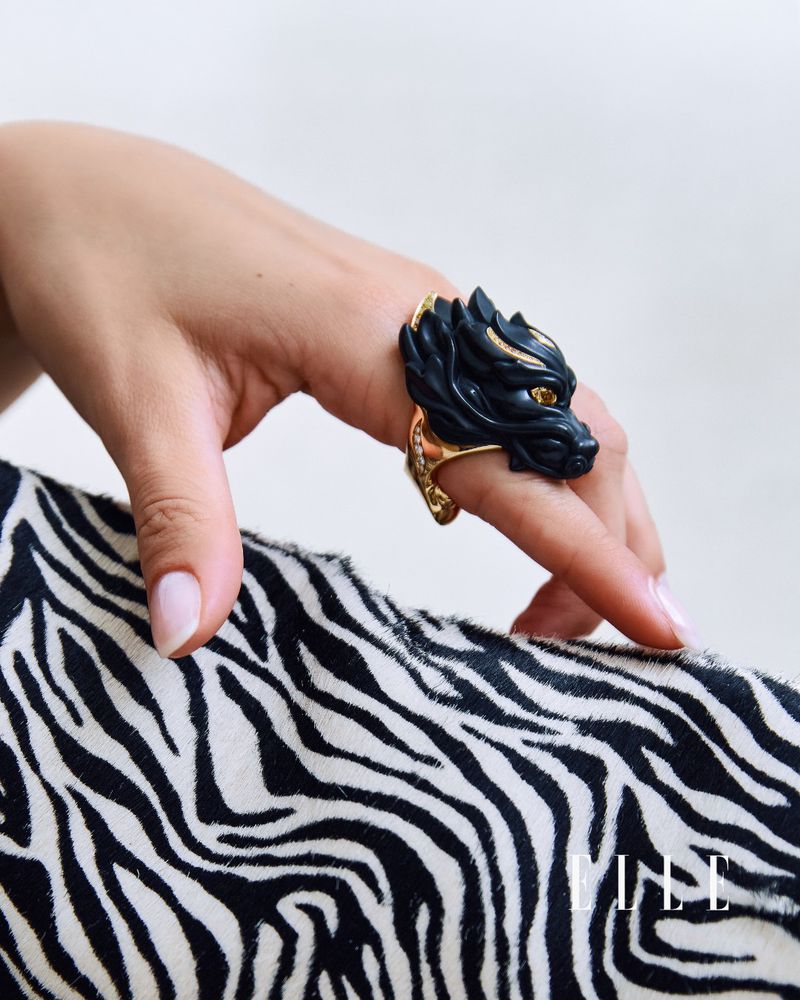 Close-up of a hand wearing an ornate black and gold animal head ring over zebra print fabric.