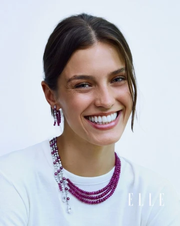 Model Emma Todt smiling in a white t-shirt wearing a multi-strand ruby beaded necklace and matching earring against a white backdrop.