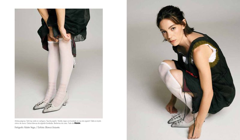 Vicky Luengo wearing a black sleeveless dress, white knee-high socks, and silver pointed kitten heels against a white backdrop.