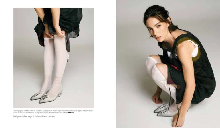Vicky Luengo wearing a black sleeveless dress, white knee-high socks, and silver pointed kitten heels against a white backdrop.