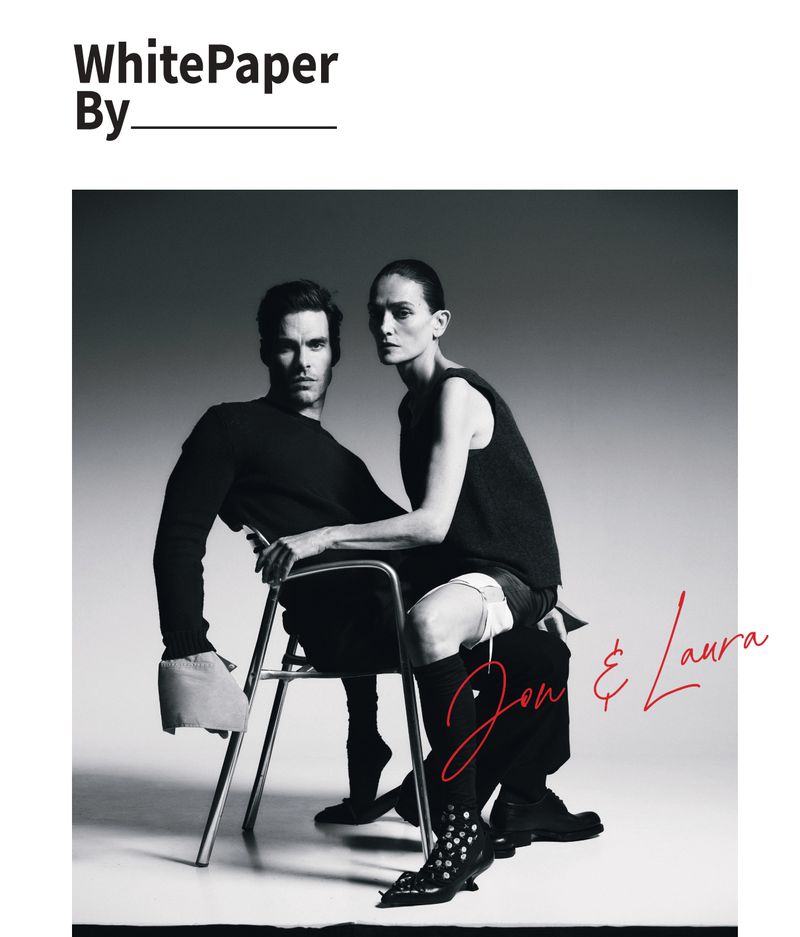 Jon Kortajarena and Laura Ponte posed together on a metal frame chair wearing black designer apparel in a studio setting.
