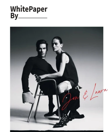 Jon Kortajarena and Laura Ponte posed together on a metal frame chair wearing black designer apparel in a studio setting.