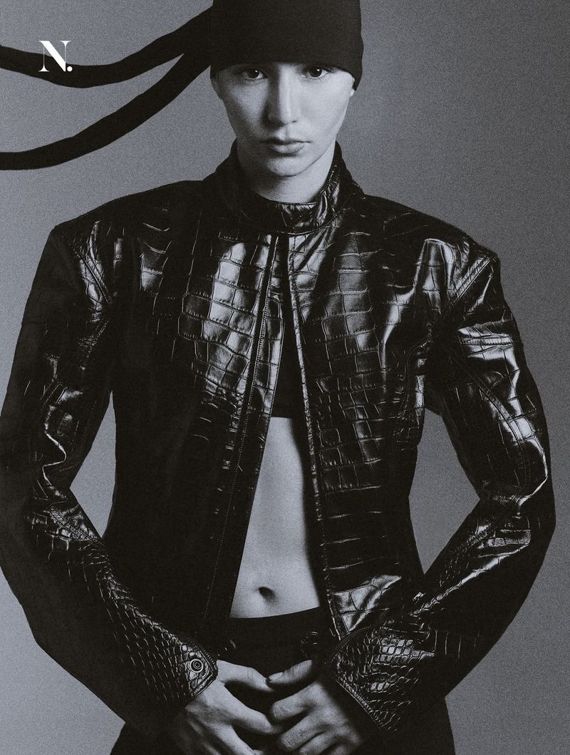 Model in a black embossed crocodile leather jacket and black headwrap against a smooth grey studio backdrop.