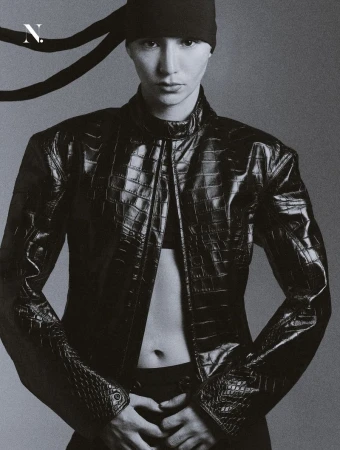 Model in a black embossed crocodile leather jacket and black headwrap against a smooth grey studio backdrop.