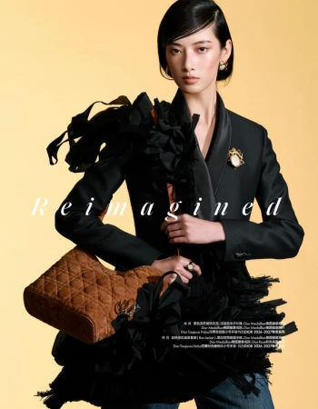 Model Cici Xiang holding a quilted brown handbag while wearing a black tailored jacket against a warm yellow studio background.