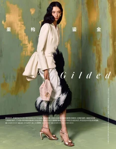 Model Cici Xiang Yejing poses in a cream structured jacket and feather-trimmed skirt against a gold and green textured wall.